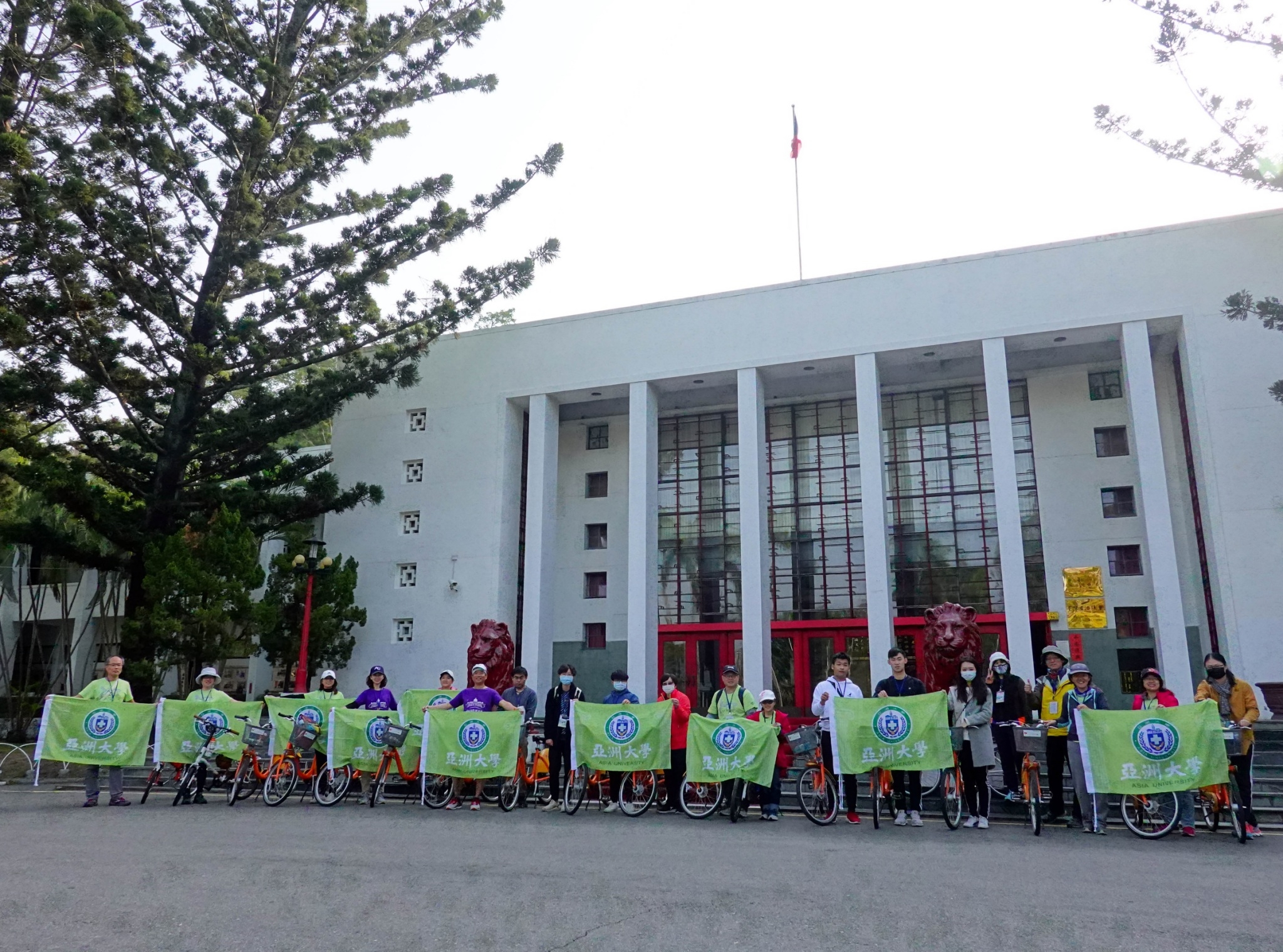 亞大主任秘書施能義(左6)與繞騎霧峰20K團隊成員拉開校旗，歡慶亞大20週年活動。