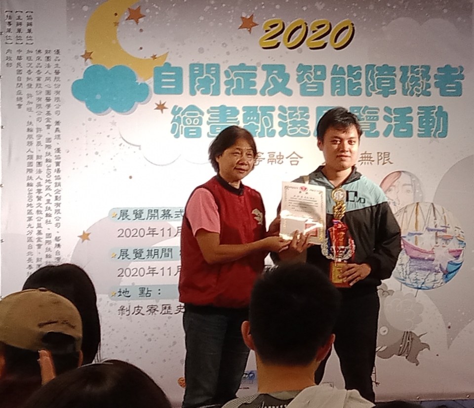 數媒系碩士生洪梓晏（右）以「愛心行動」作品，獲全國性身心障礙繪畫比賽成人組佳作，接受頒獎表揚。