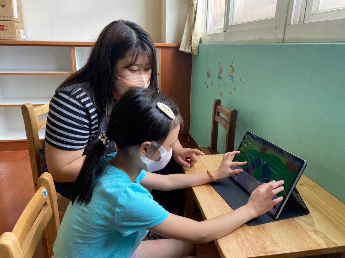 图为亚大幼教系同学，指导小朋友用双手操作电子绘本，探讨他们的阅读理解表现