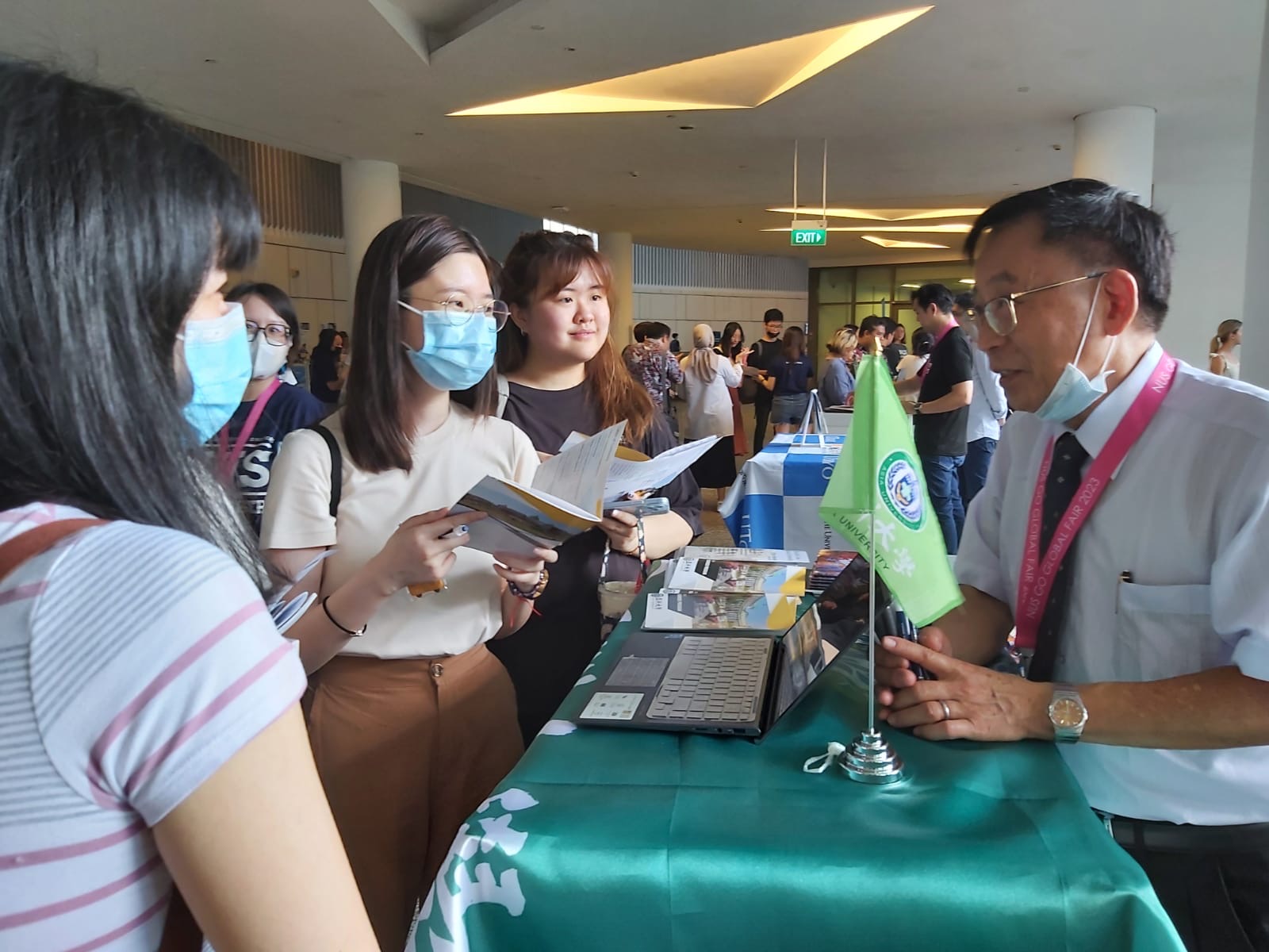 图为亚大国际学院长陈英辉(右1)，在国立新加坡大学的夏日学校博览会，向该校学生说明亚大暑期课程。