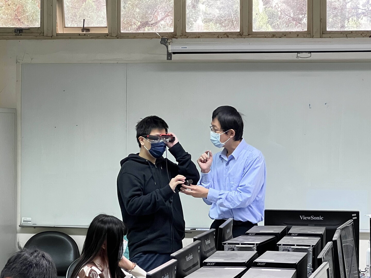 圖為亞大資工系在資訊體驗中,謝長倭老師(右)教導高中生,使用AR眼鏡。