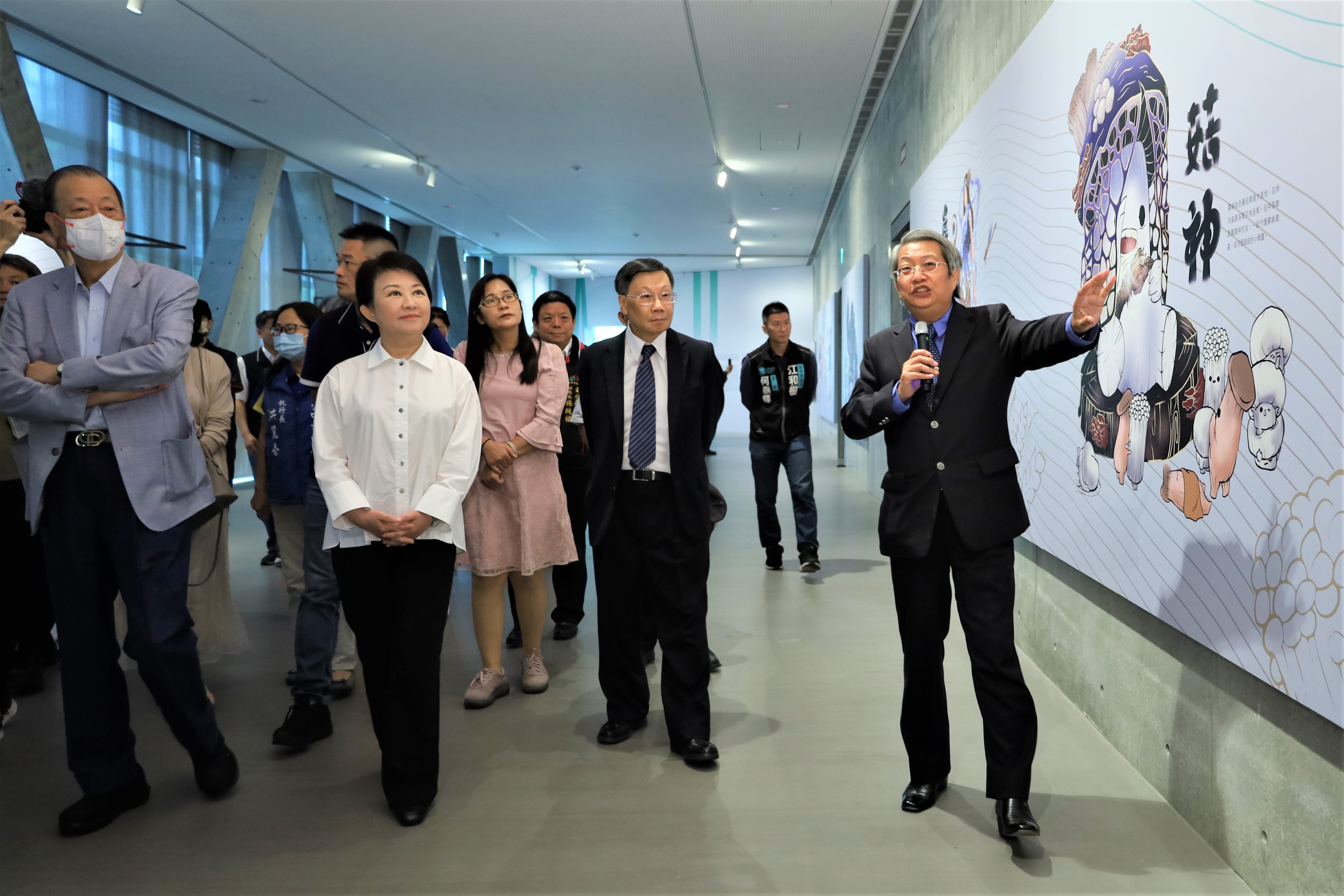 台中市长卢秀燕（左前二）、亚大创办人蔡长海（左前一）、亚大校长蔡进发（左前三）与贵宾，听取亚大现代美术馆馆长潘襎（右）介绍视传系学生创作获国际大奖10神仙的菇神。