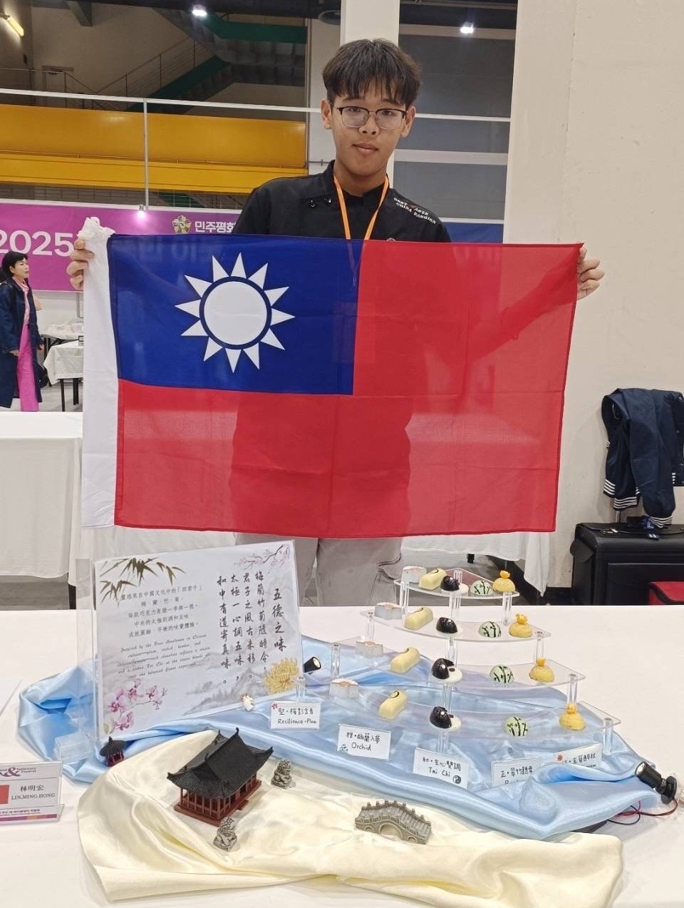 亞大護理系林明宏同學拿國旗,與他的得獎作品「五德之味」合影。