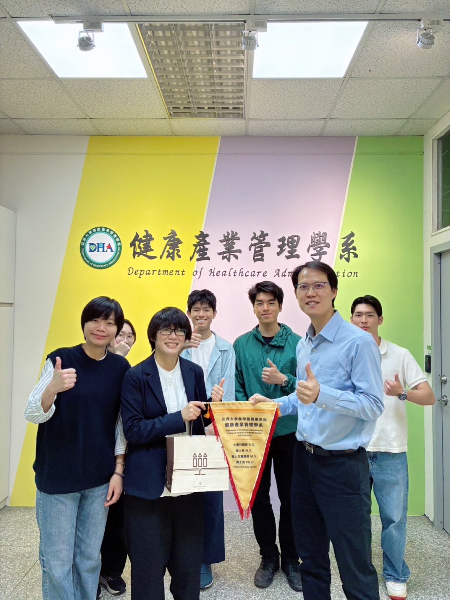 亞洲大學健康產業管理學系王俊毅副主任(前右)代表學系,致贈校旗予日本神戶大學余玟欣助理教授(前中),象徵兩校學術情誼的建立與交流活動正式啟動。