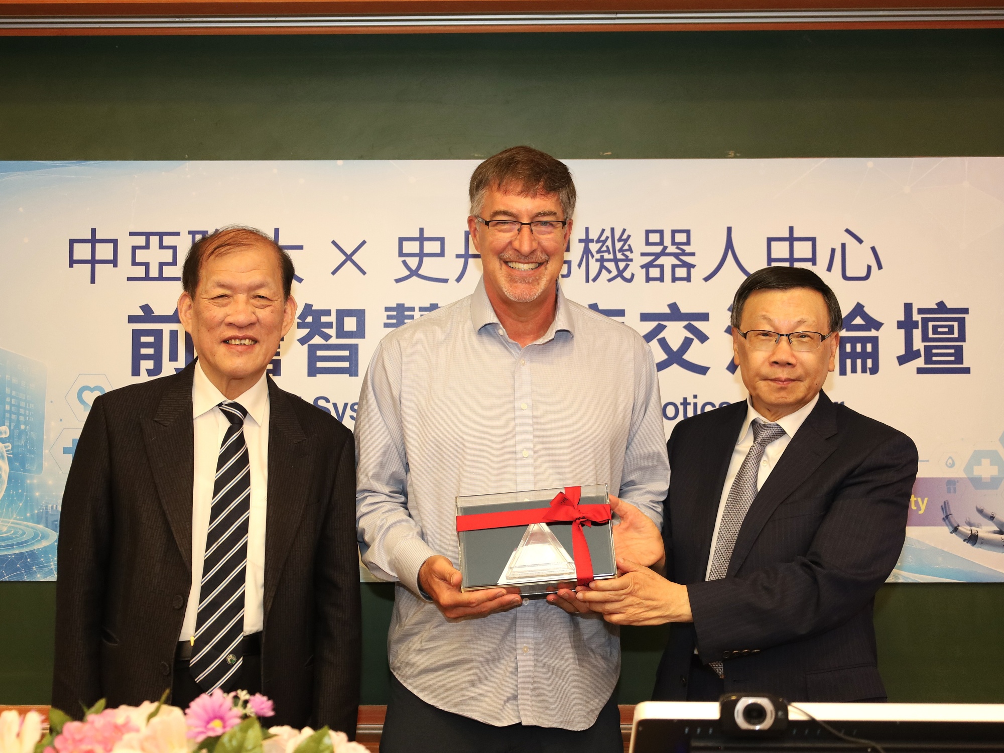 Asia University President Jeffrey J.P. Tsai (right) presents a commemorative gift to Dr. Steve Cousins of Stanford (center)
